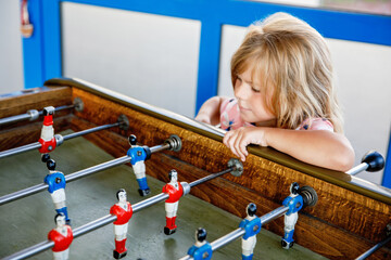 Little preschool girl playing table soccer. Happy excited positive child having fun with family...