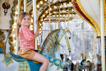 Happy positive preschool girl having a ride on the old vintage merry-go-round in city of St Malo France. Smiling child on a horse. - obrazy, fototapety, plakaty