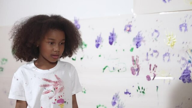 Young asian boy running to stamp colored hand print at cute african girl shirt. Student playing in art lesson with white background stained with colorful color. Creativity activity concept. Erudition.