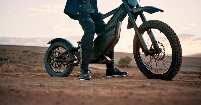 Biker, electric bike and man with gear in outdoor training to start for extreme sports, safety and practice on sand. Legs, ready or driver with helmet for dunes, race or cycling in challenge in rally