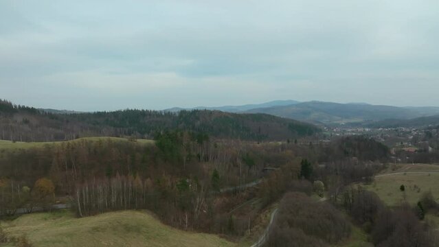 Aerial backwards shot of hilly forest landscape during cloudy day in Poland. Wide shot.