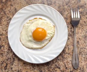 Fried egg on a white plate with a fork on the table