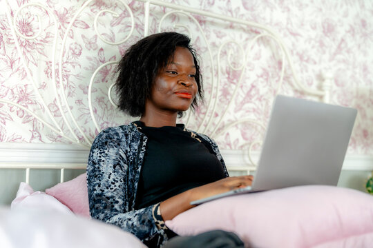 Woman working on laptop while sitting on bed, comfortable home setting with a focused expression.