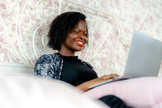 Serious young woman working from bed with laptop, a representation of the modern, flexible workplace