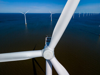 A mesmerizing view of wind turbines peacefully spinning in the ocean, creating renewable energy in the vibrant Spring season of Flevoland, Netherlands. windmill turbines green energy in the ocean - obrazy, fototapety, plakaty