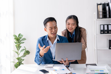 Two young asian business people using a laptop together while sitting in a meeting.