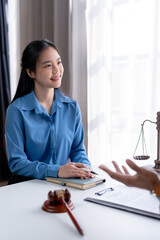 Smiling asian female client in a blue shirt during a consultation with her attorney in law office.