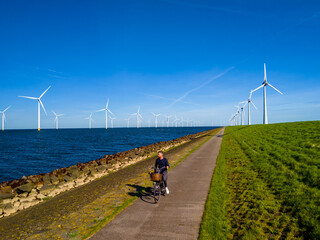 A man rides an electric bike down a picturesque path next to a serene body of water with windmill turbines in the distance, enjoying the beauty of nature in the Netherlands Flevoland during Spring.