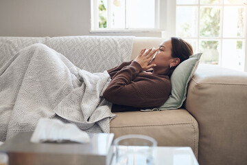 Sick woman, sneeze and blowing nose with flu, cold or illness on living room sofa at home. Young...