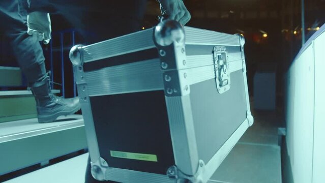 Man walks along stage and carries metal toolbox. Professional guy carries necessary tools for work in heavy construction suitcase