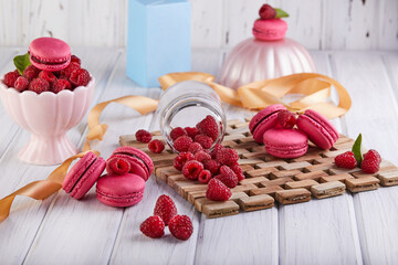 A stack of pink macarons surrounded by raspberries on a wooden table