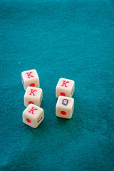Dice for playing poker, with four figures of the king and one of the queen, on a green mat.
