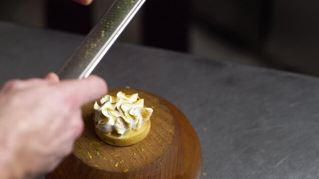 Grating lemon zest on a small lemon cake decorated with fluffy mousse. Professional pastry art in slow motion