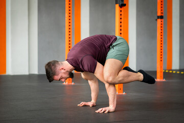 Strong man performing calisthenics frog stand exercise in gym