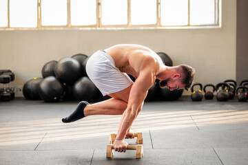 Fit man performing Tuck planche calisthenics exercise in fitness club