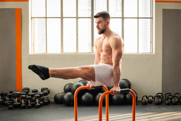 Man performing L sit on parallel bars calisthenics exercise in fitness club