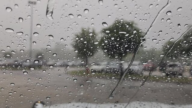 This is a short video clip of rain, falling onto a car window, creating large droplets and small streams of water, flowing down the window.