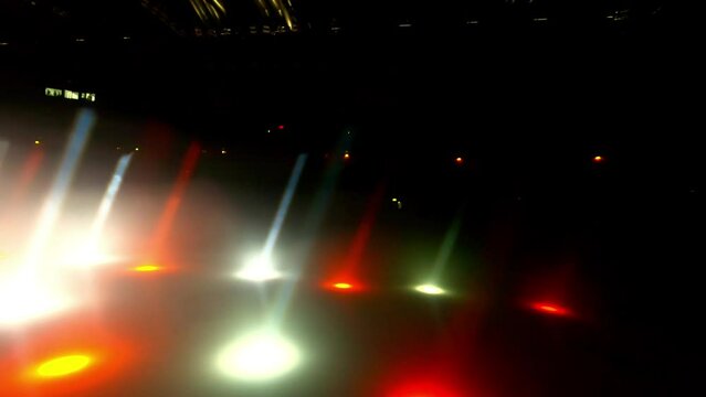 White and red beams of light twinkle in darkness of stage. Interplay of lights creates sense of rhythm and motion during performance