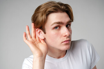 Young Man Placing Hand Behind Ear to Listen More Attentively Against a Neutral Background