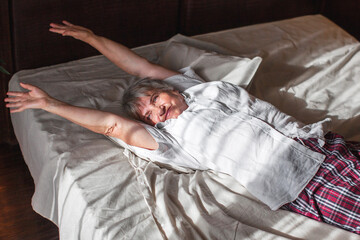 Senior woman stretching in bed waking up at home