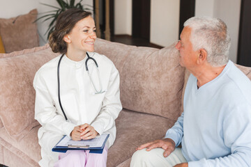 Female professional doctor showing medical test result explaining prescription using clipboard visiting senior elderly old man patient at home sitting on sofa - 781102662