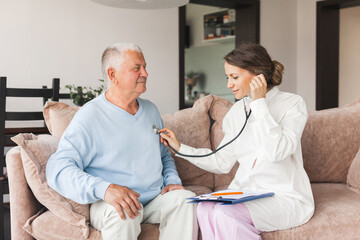 Woman nurse doctor gp holding stethoscope examining old senior 60s grandpa patient check heartbeat at home care checkup medical visit