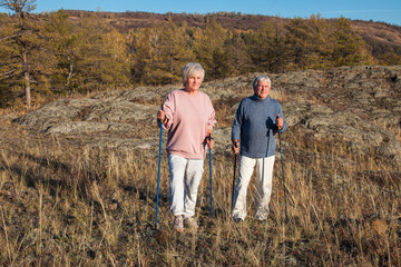 Happy middle age woman and man walking with Scandinavian sticks in autumn forest - 781103003