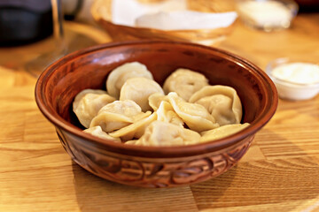 Fresh tasty dumplings in brown carved clay bowl with sour cream. Home comfort or restaurant menu and serving