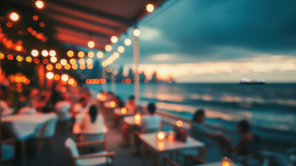 Blurred image shows bokeh of lights of a restaurant on a promenade by the sea. Unknown people are sitting at tables by candlelight. The sea, sunset and a ship can be seen in the background.