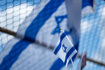 A person holds up a small Israeli flag at a pro-Israel demonstration. In the background, a large...