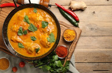 Tasty chicken curry with parsley and ingredients on wooden table, flat lay. Space for text