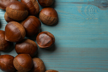 Roasted edible sweet chestnuts on light blue wooden table, flat lay. Space for text