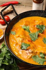 Tasty chicken curry with parsley and ingredients on wooden table