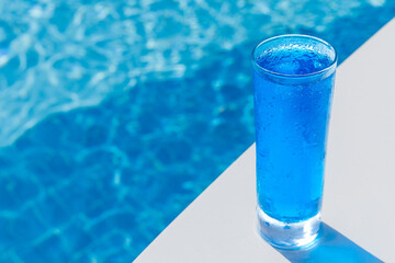 A glass of delicious blue cocktail Blue Lagoon on the background of the pool. Alcoholic cocktail juicy fruit blue with curacao liqueur, ice cubes