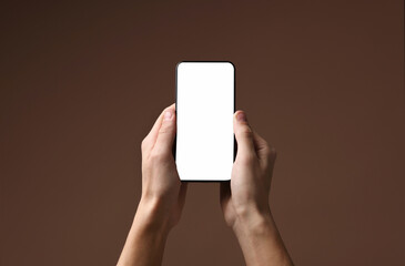 Fototapeta na wymiar Man holding smartphone with blank screen on brown background, closeup. Mockup for design