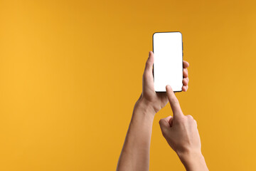 Man using smartphone with blank screen on yellow background, closeup. Mockup for design