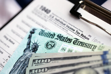 United States 1040 tax form individual income tax return with refund check and US dollar bills close up