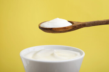 Eating delicious natural yogurt on yellow background, closeup