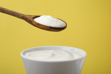 Eating delicious natural yogurt on yellow background, closeup