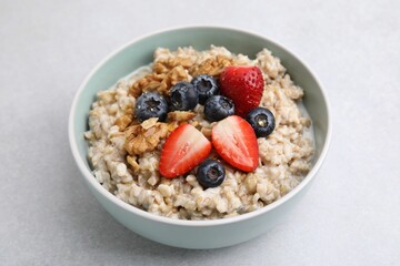 Tasty oatmeal with strawberries, blueberries and walnuts in bowl on grey table