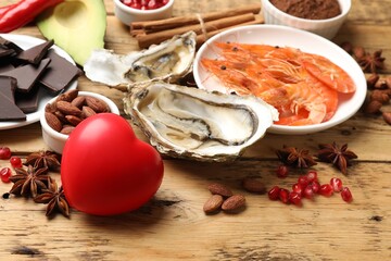 Natural aphrodisiac. Different food products and heart model on wooden table, closeup