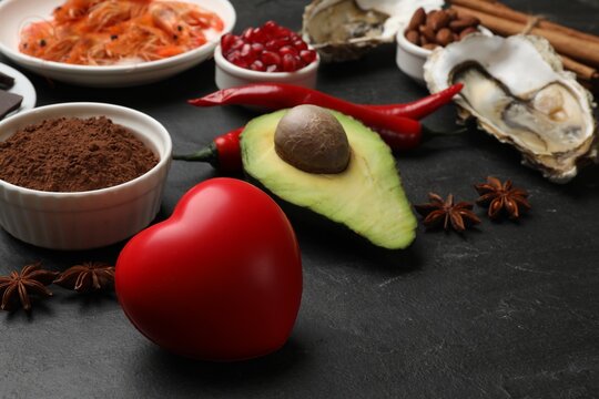 Natural aphrodisiac. Different food products and heart model on black table, closeup