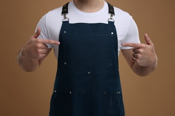 Man pointing at kitchen apron on brown background, closeup. Mockup for design