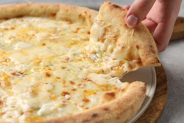 Woman taking piece of delicious cheese pizza at light grey table, closeup