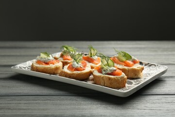 Tasty canapes with salmon, cucumber, cream cheese and dill on wooden table