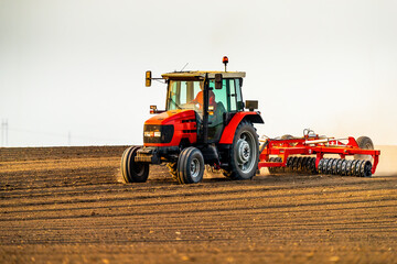 Powerful tractor tills agricultural land as the sun sets, creating a scenic farm landscape