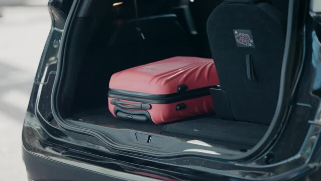 Coral suitcase in open car trunk at the airport