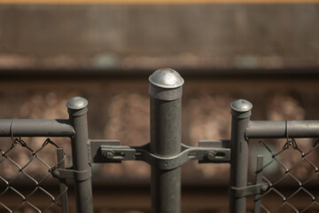 Closeup of the top of a chain link fence. in the defocused background, a train track is visible.