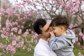 dad and son hugging against blossom pink tree in park. loving father with baby boy kid.happy fathers day holiday.spring time,easter is coming