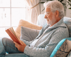 Senior bearded smiling man sitting on sofa reading a book - indoor, at home concept - caucasian...